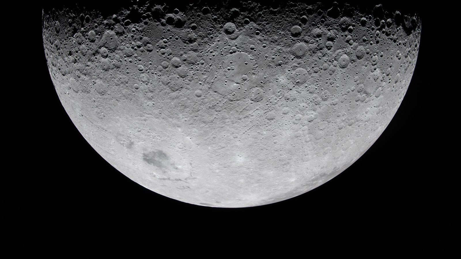 Disco lunar parcialmente iluminado, visto de perto pela tripulação do Artemis II: o terminador atravessa o topo do quadro, com crateras a recortarem-se como ilhas na sombra e cadeias de crateras a estenderem-se pelo terreno iluminado; fundo negro