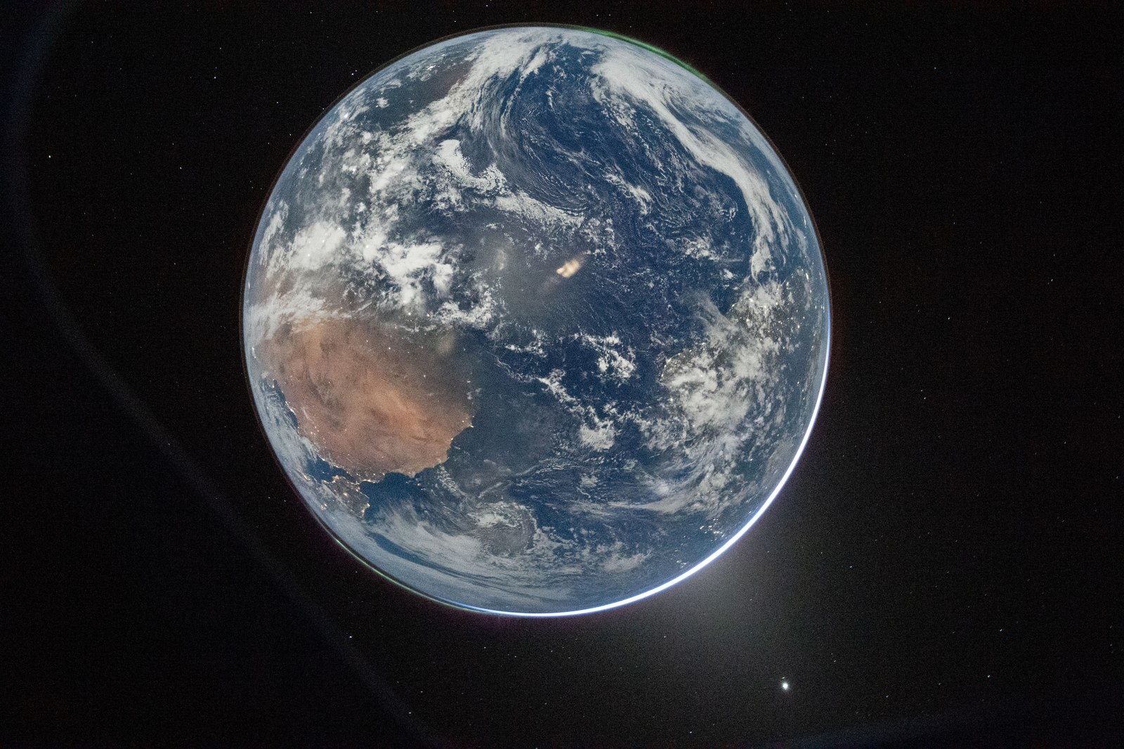Disco completo da Terra visto do espaço: o Sara e o Norte de África em tons acastanhados, o Mediterrâneo e a Europa sob nuvens, um halo luminoso no bordo direito e fundo negro com estrelas