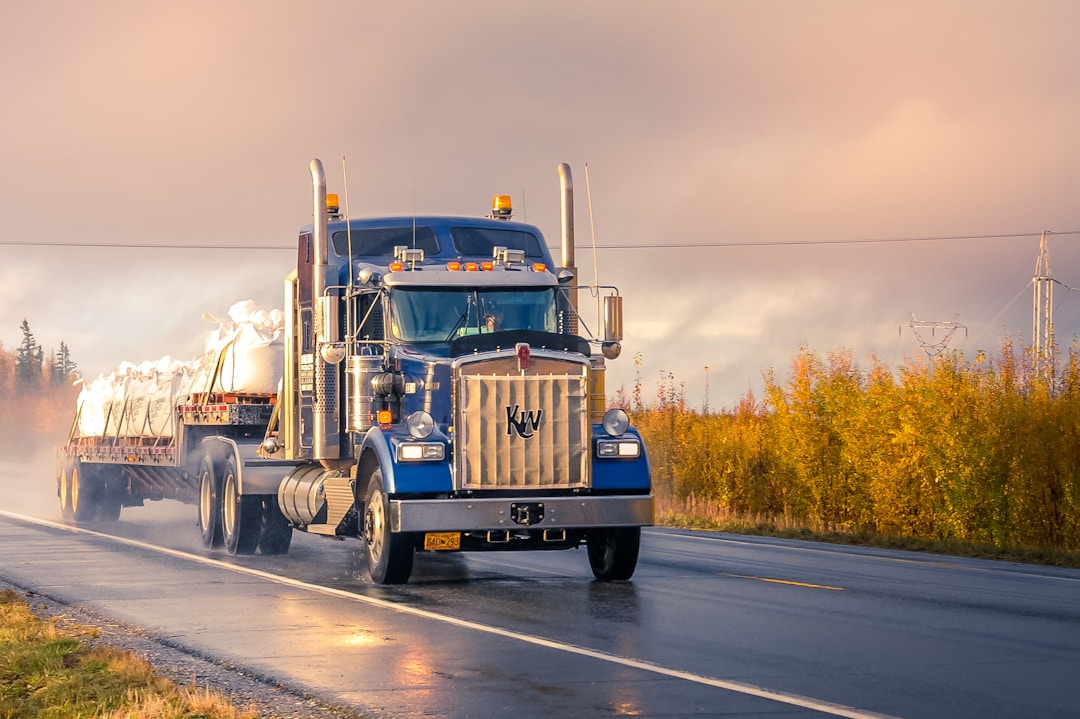 Camião Kenworth azul a circular numa estrada outonal, rebocando uma plataforma com carga — o transporte rodoviário de mercadorias é um dos maiores consumidores de diesel do mundo