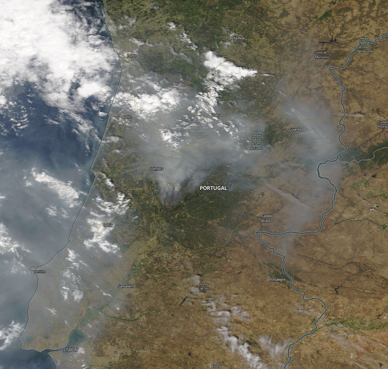 Imagem de satélite de Portugal com nomes de cidades sobrepostos e uma vasta camada de fumo a atravessar o centro do território, de Coimbra para leste, em tons de cinzento-claro sobre o verde e o castanho do terreno.