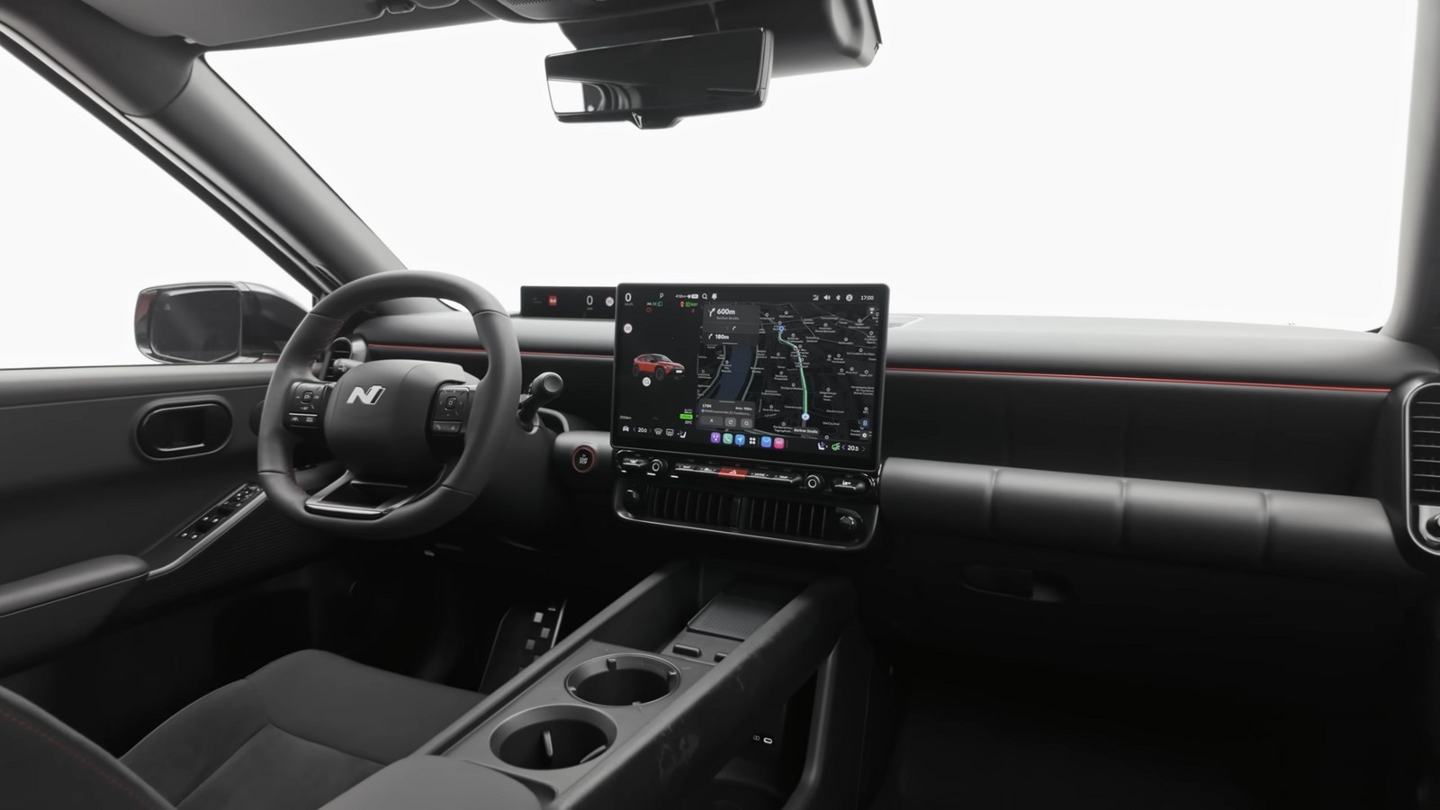 Interior de um automóvel visto do lugar do condutor: volante de três raios com logótipo N ao centro, ecrã central vertical com um mapa de navegação, painel digital estreito atrás do volante, linha vermelha a atravessar o tabliê e consola central com dois porta-copos.