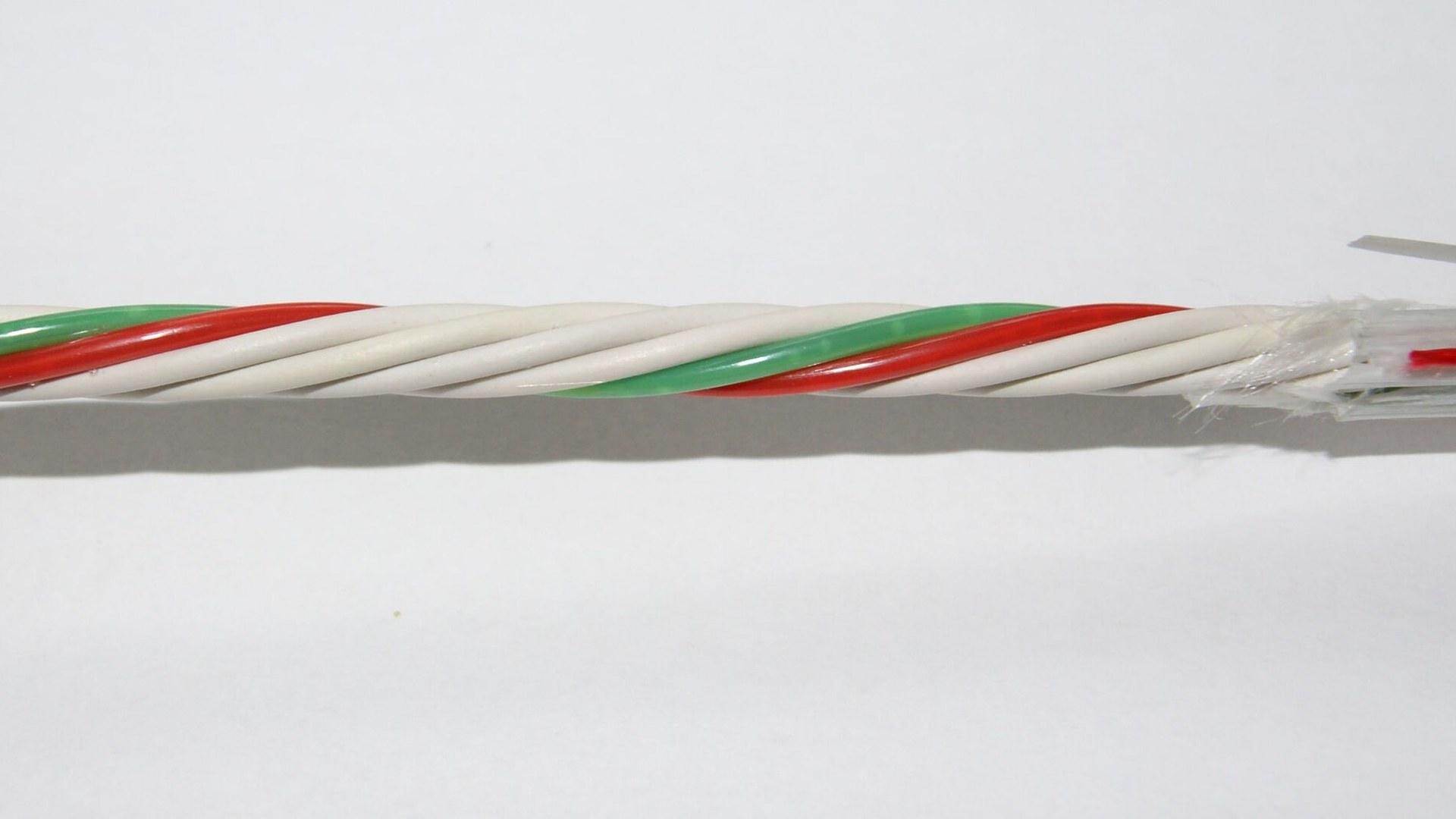 Cabo de fibra óptica aberto sobre fundo branco, com pares coloridos — verde e vermelho — torcidos em torno de um núcleo de elementos brancos, e a capa exterior descarnada à direita