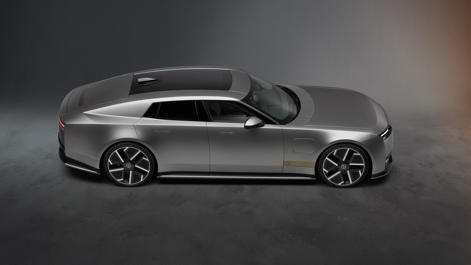 Perfil lateral do Jaguar Type 01 prata num fundo de estúdio escuro: capô longo, tejadilho baixo, portas sem puxadores salientes e jantes de 23 polegadas.