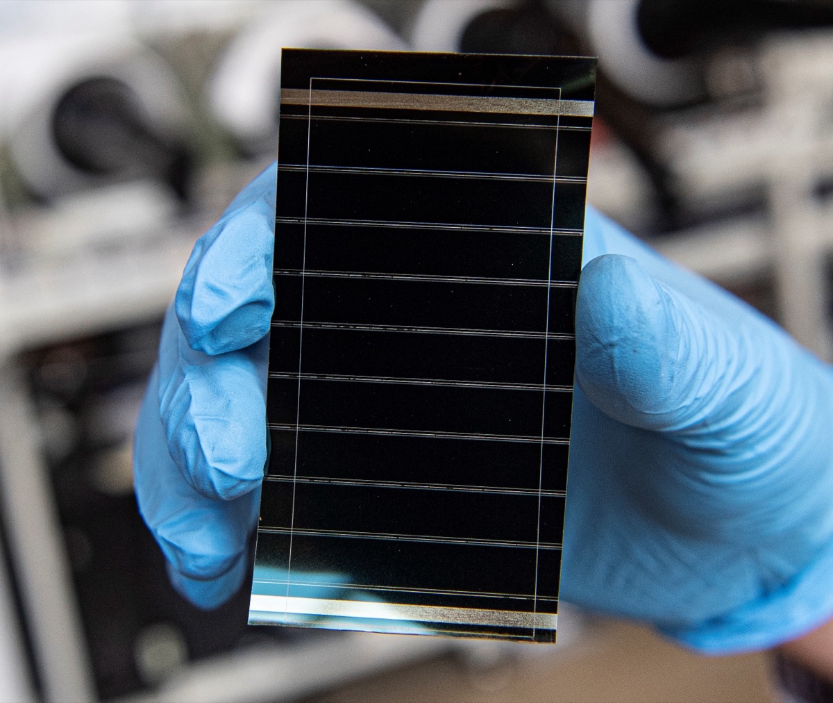 Investigador do NREL segura uma célula solar de perovskita num laboratório — o material que permite às células tandem ultrapassar os limites do silício