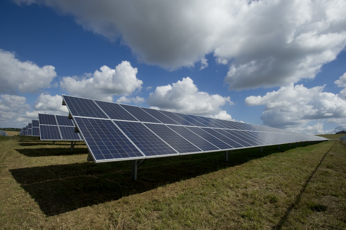 Parque fotovoltaico de grande escala com fileiras de painéis solares a estenderem-se até ao horizonte sob um céu azul com nuvens