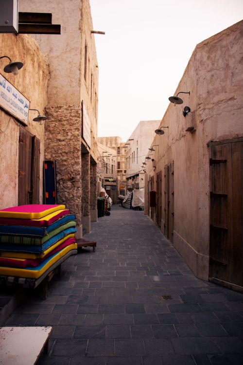 Beco estreito de um souq tradicional de arquitetura histórica do Médio Oriente, com paredes de pedra e têxteis coloridos