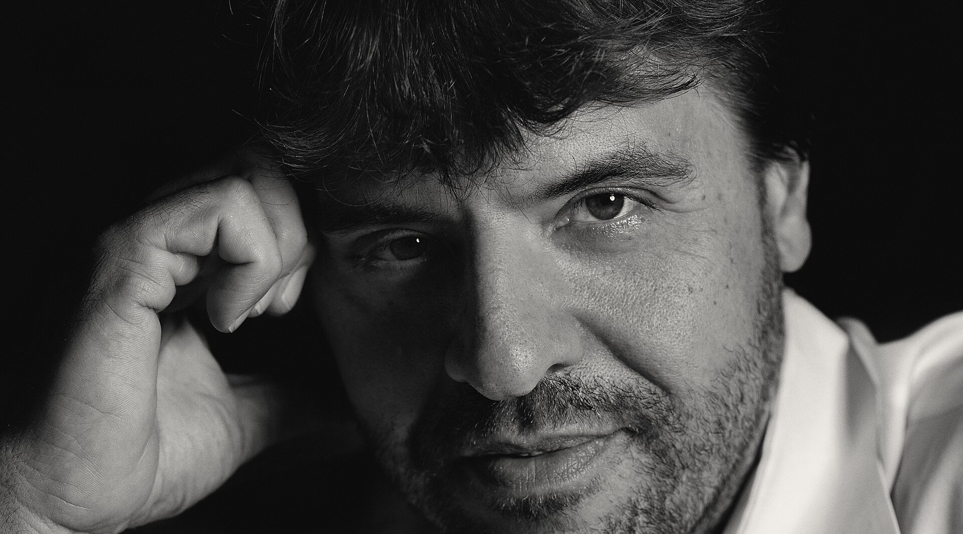 Retrato a preto e branco de Karl Deisseroth, de camisa branca e barba curta, com a mão apoiada na têmpora, sobre fundo escuro