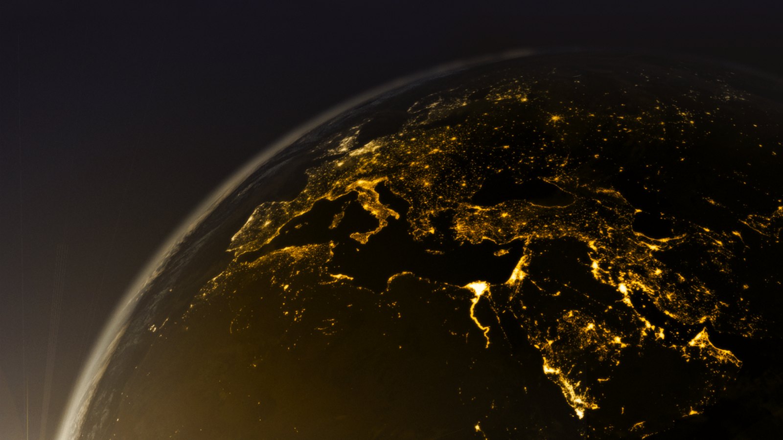 Vista orbital da Europa de noite, com as cidades iluminadas a amarelo-ouro e a atmosfera como um fino arco azulado no limbo do planeta