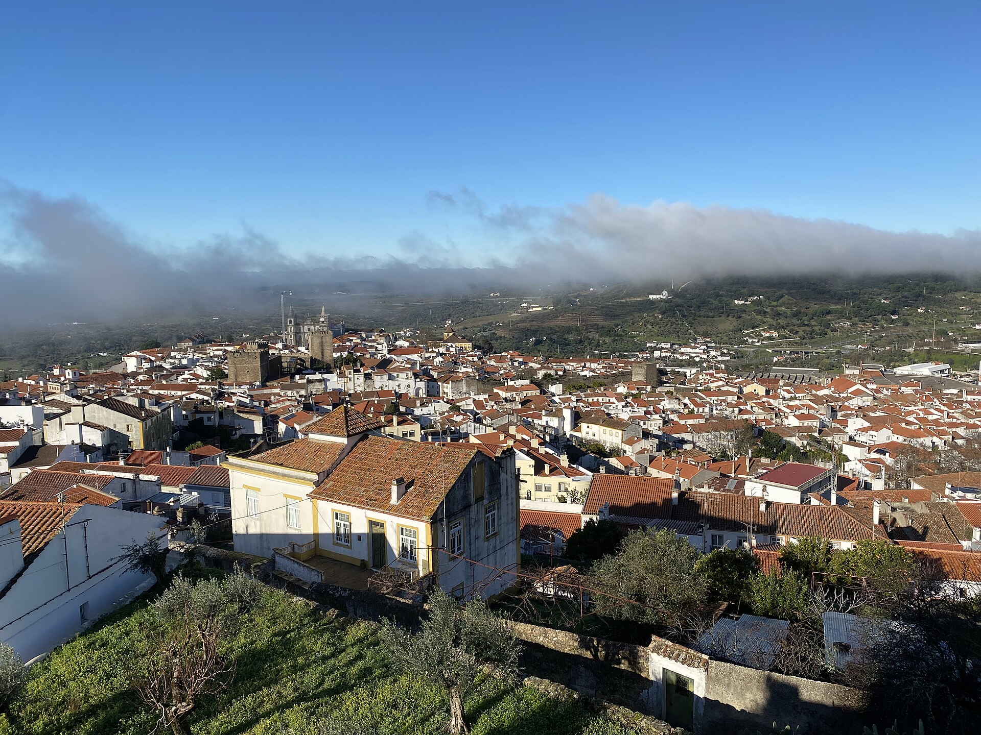 Vista sobre os telhados de Portalegre ao início da manhã, com as torres da Sé ao centro e nevoeiro sobre a Serra de São Mamede ao fundo.