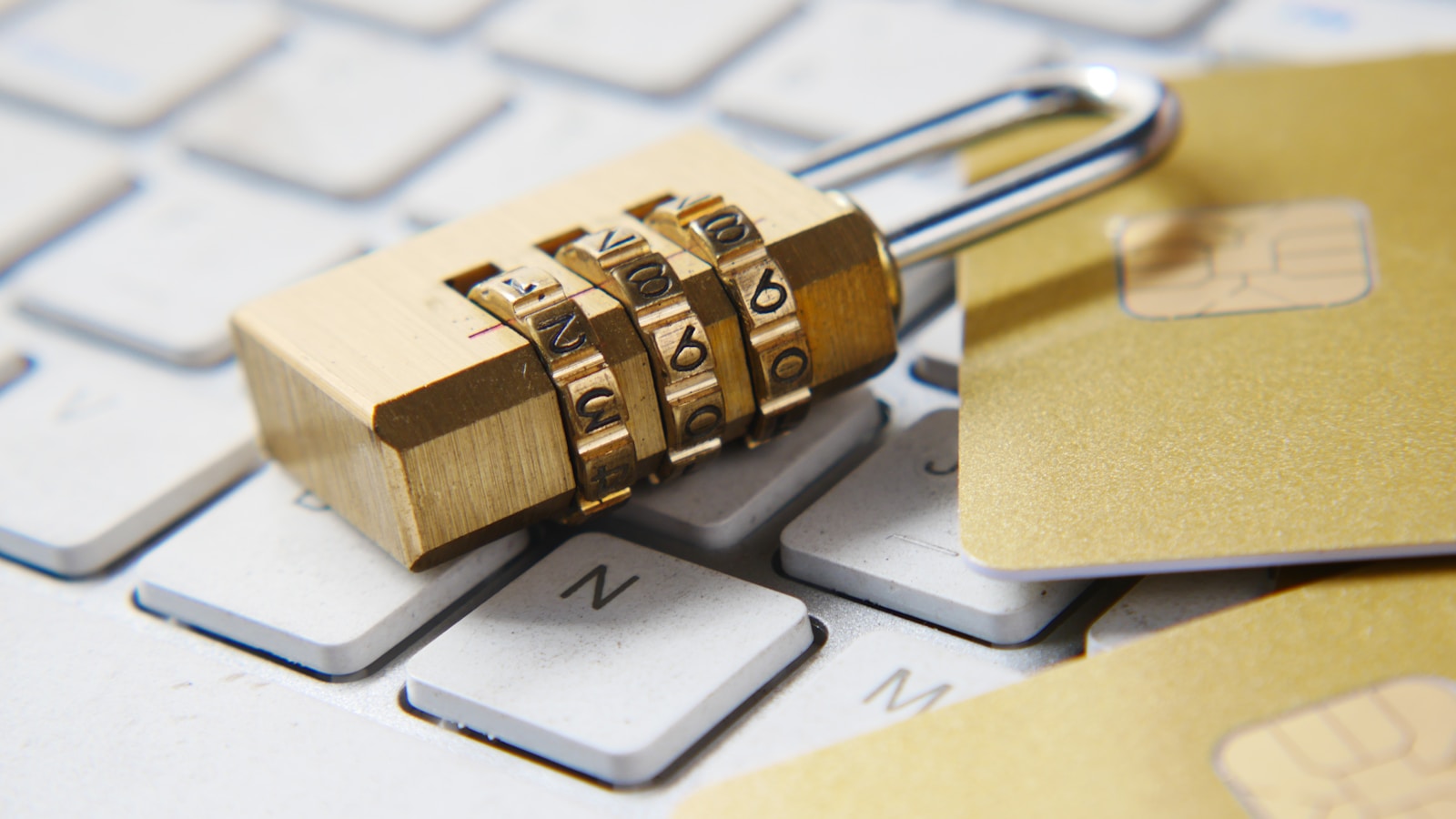 Cadeado dourado de combinação sobre um teclado de computador, com cartões de crédito com chip ao lado — símbolo da proteção de dados digitais e privacidade online