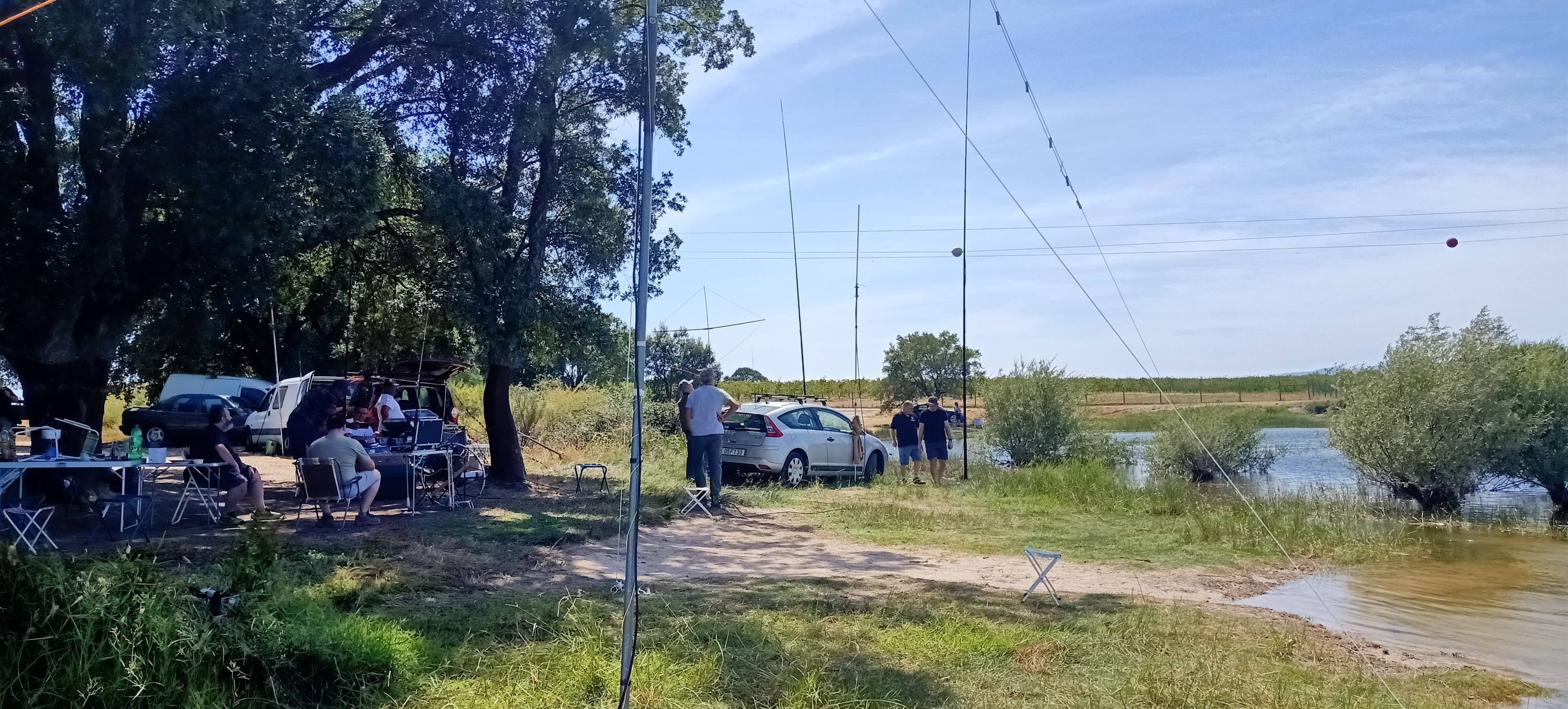 Operação de campo de radioamadores da ARBB junto a um rio, com antenas verticais e estações portáteis montadas