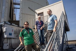 Três investigadores junto a uma instalação técnica exterior de Brookhaven