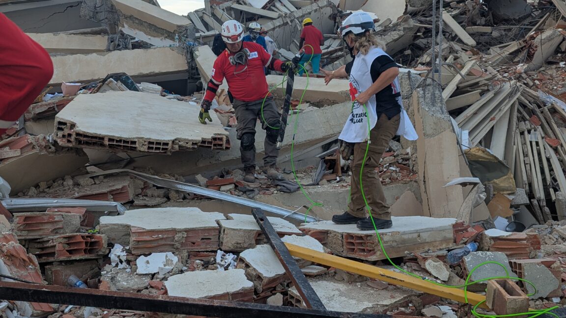 Socorristas da Brigada Internacional de Resgate Topos Azteca operam o robot-cobra da Carnegie Mellon entre os escombros de La Guaira, Venezuela, em julho de 2026. Cabo verde visível liga o robot ao operador.