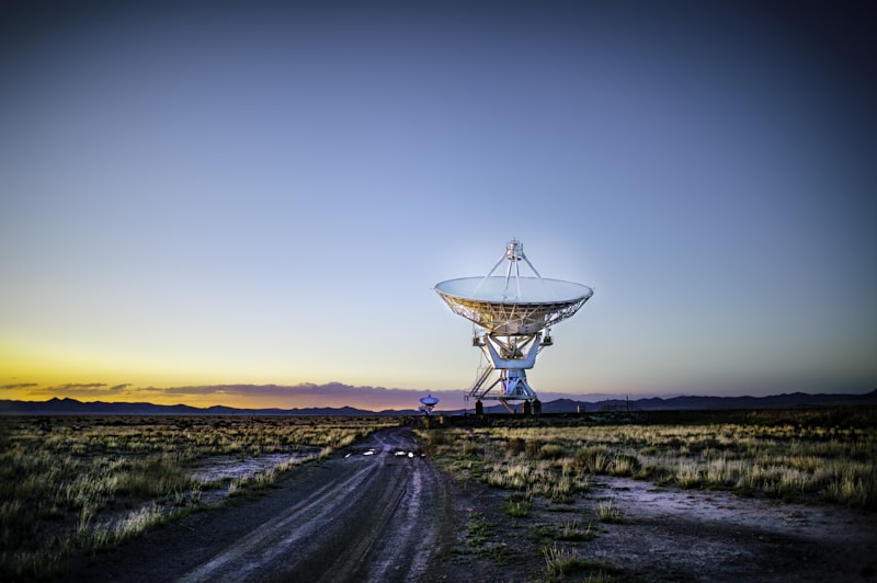 Telescópio de rádio branco num campo relvado, representando os observatórios que monitorizam a linha de hidrogénio nos 1420 MHz