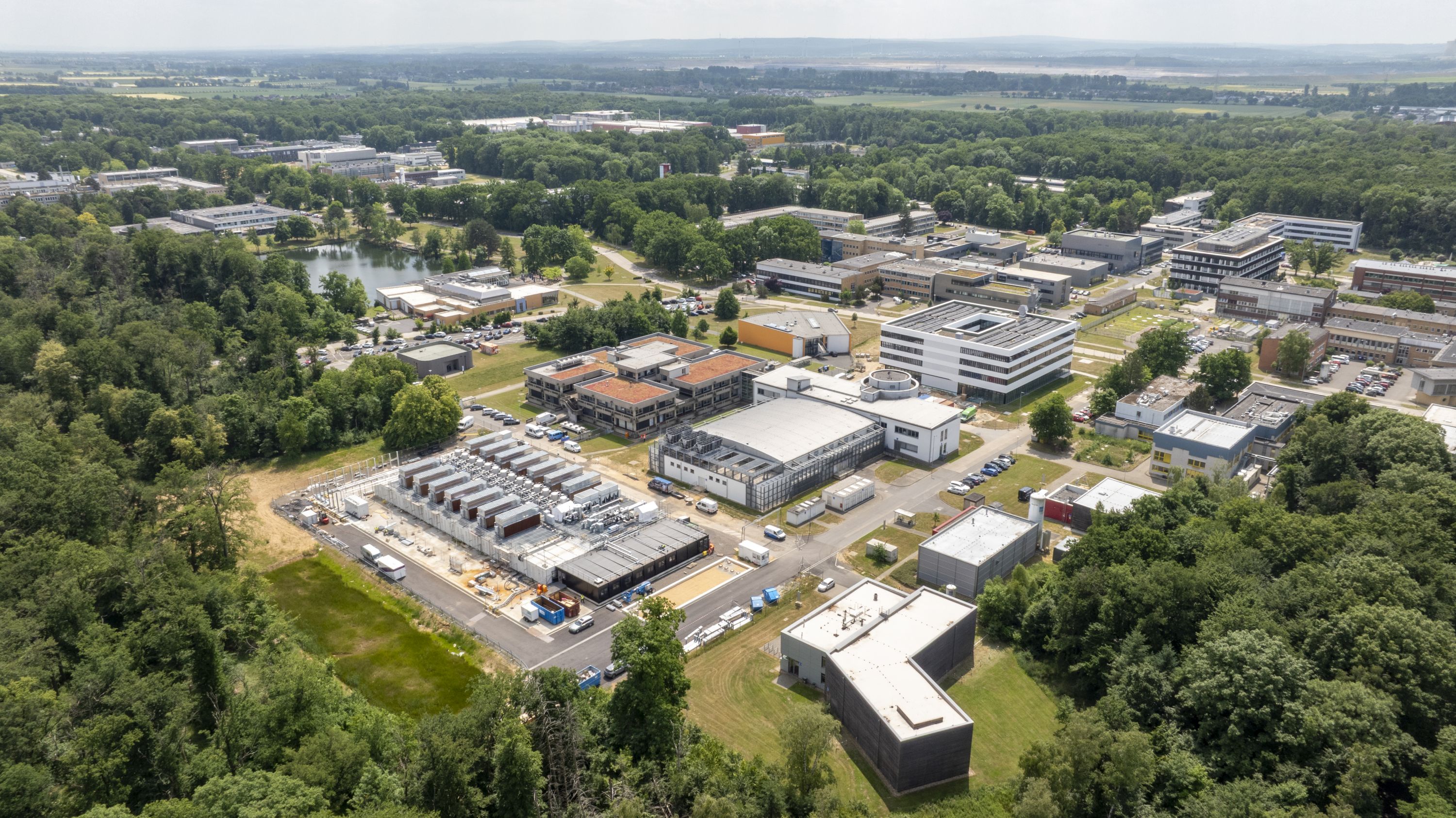 Vista aérea do campus do Forschungszentrum Jülich, com edifícios de investigação rodeados por floresta; à esquerda fica o centro modular de dados do JUPITER.