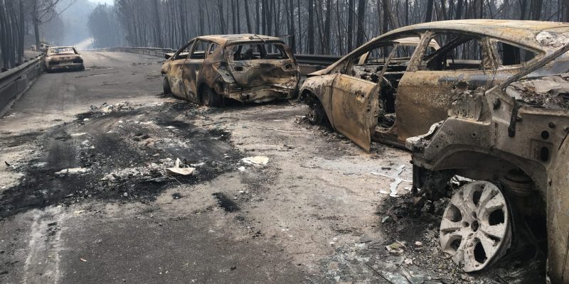 Mão de bombeiro com telemóvel num cenário de incêndio — ao lado, um rádio TETRA em silêncio