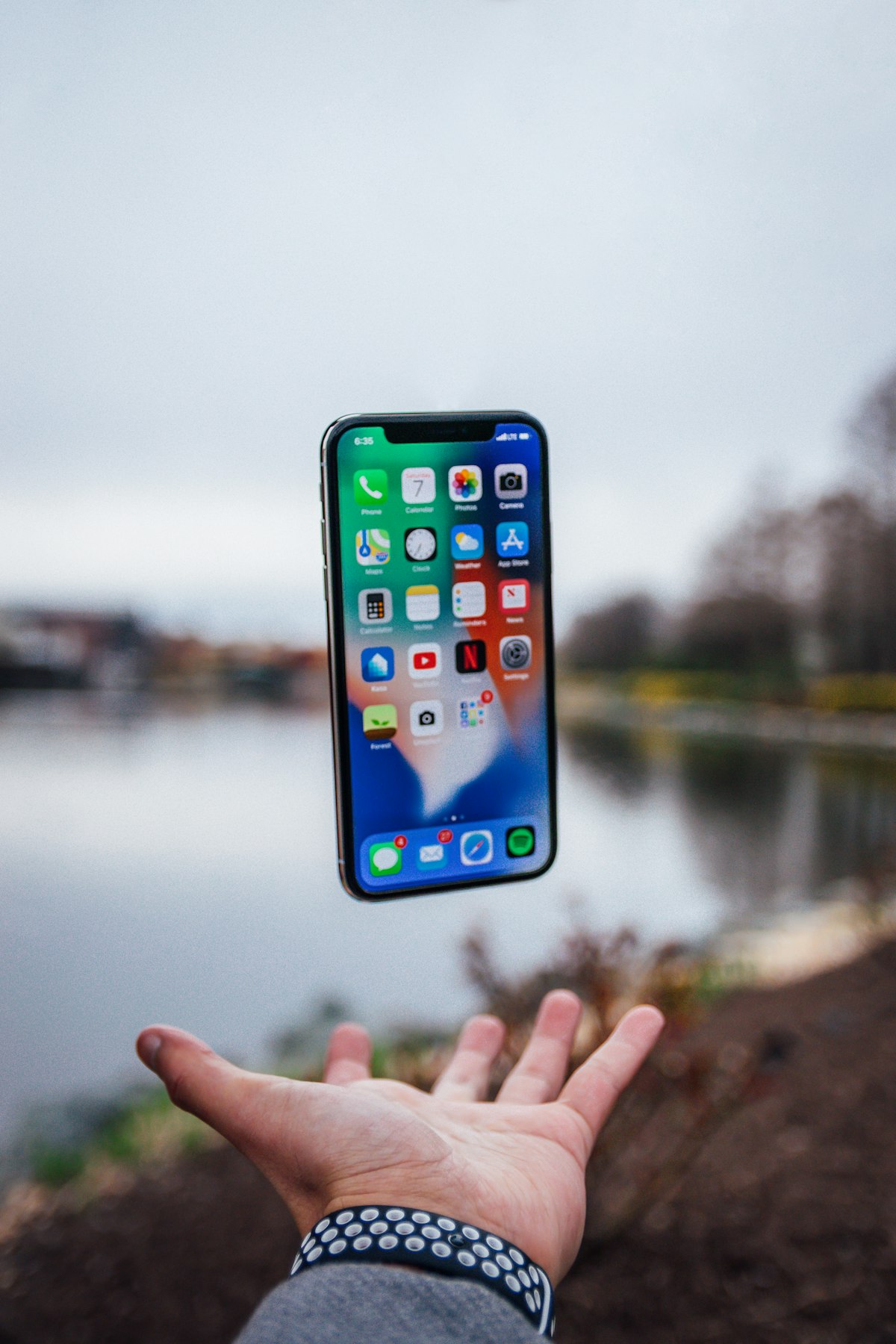 Smartphone iPhone suspenso sobre uma mão aberta, simbolizando a conectividade móvel global