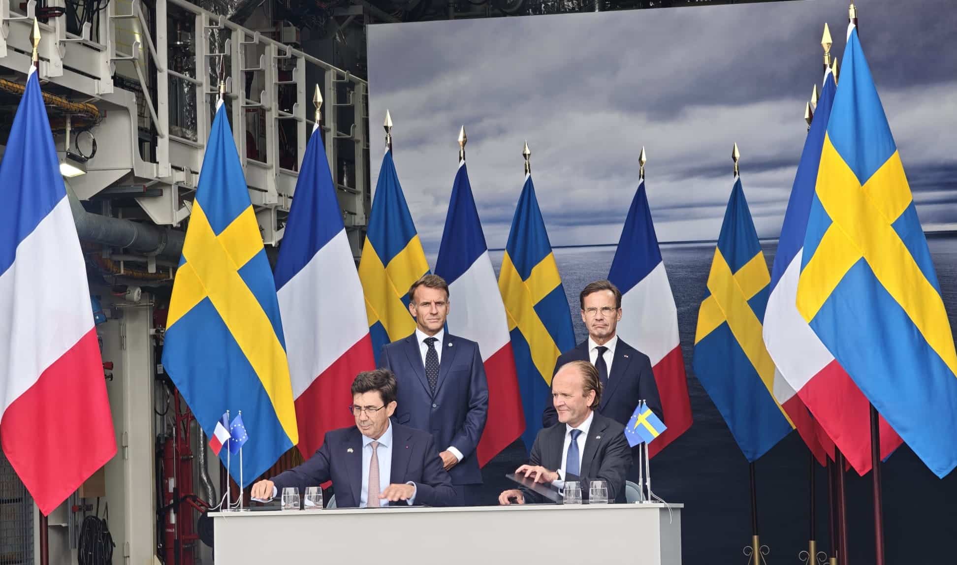 Cerimónia com bandeiras da Suécia e de França e quatro representantes junto a uma mesa