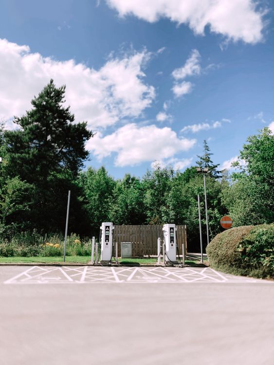 Posto de carregamento Tesla Supercharger numa zona verde e arborizada, com duas colunas de carregamento e lugares de estacionamento dedicados