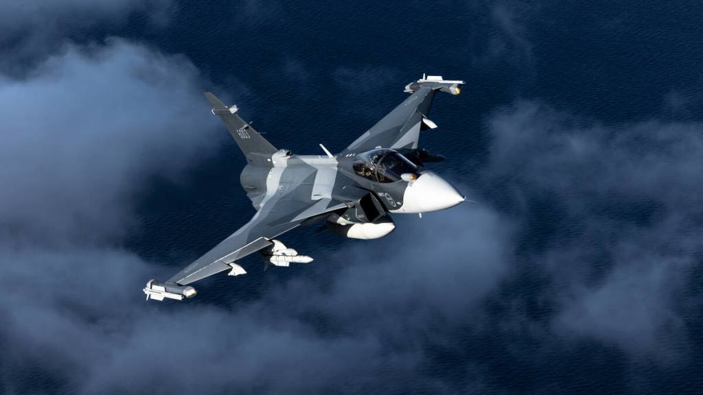 Caça Saab Gripen E em voo sobre o oceano, armado com mísseis ar-ar IRIS-T e Meteor e tanque de combustível externo — o perfil de combate que a Ucrânia vai receber