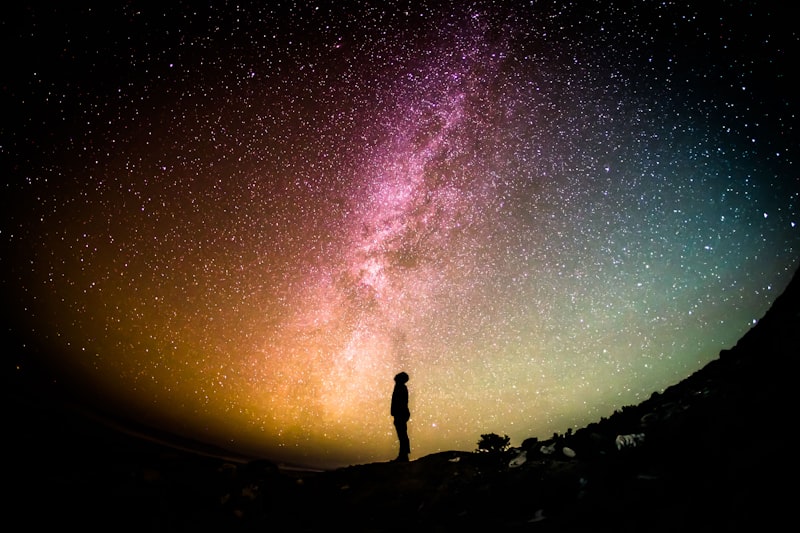 Silhueta de uma pessoa a observar o céu noturno estrelado com a Via Láctea visível
