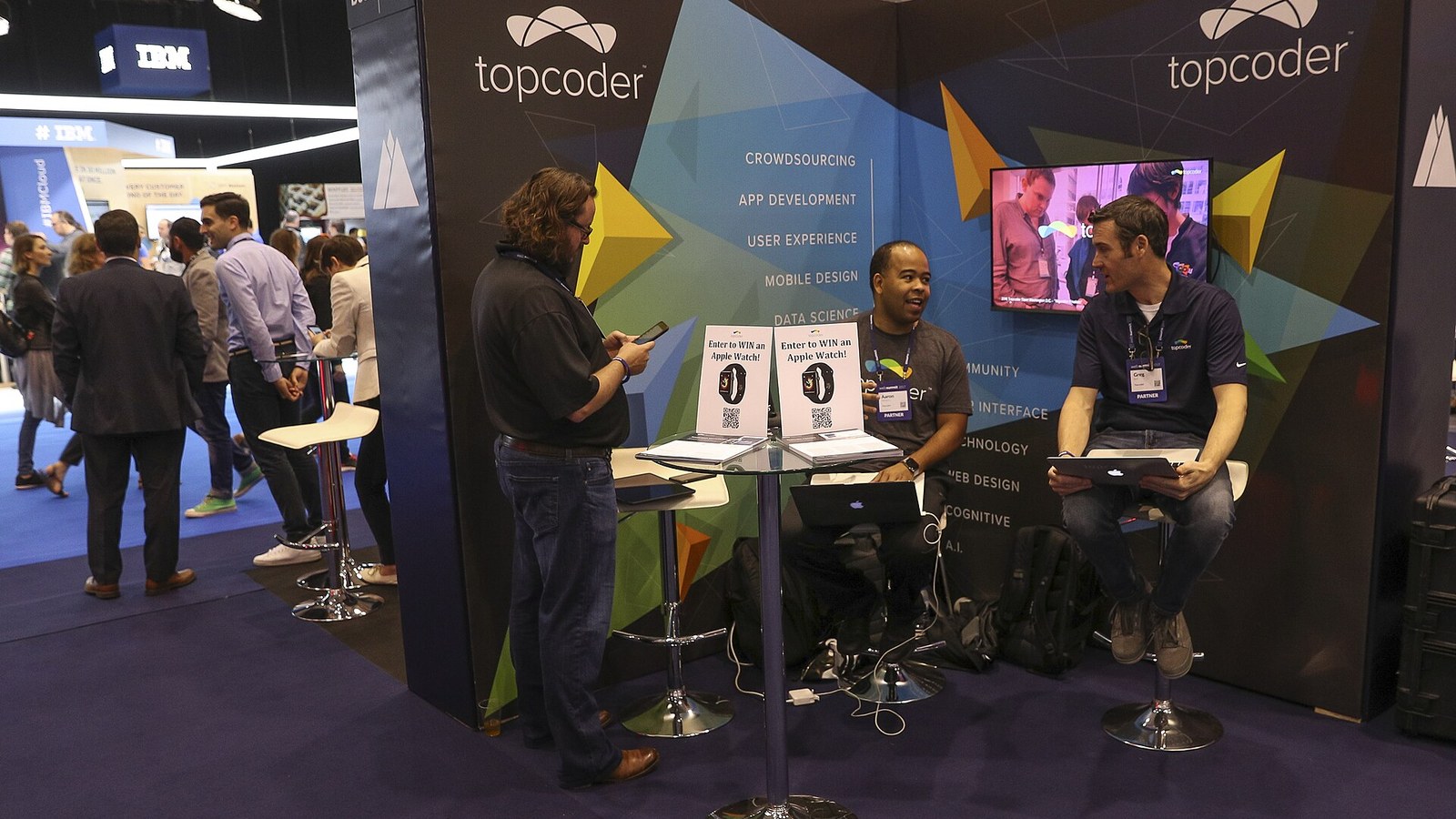 Espaço de exposição do Web Summit na Feira Internacional de Lisboa, com visitantes junto a um stand e uma câmara de Apple Watch em exposição